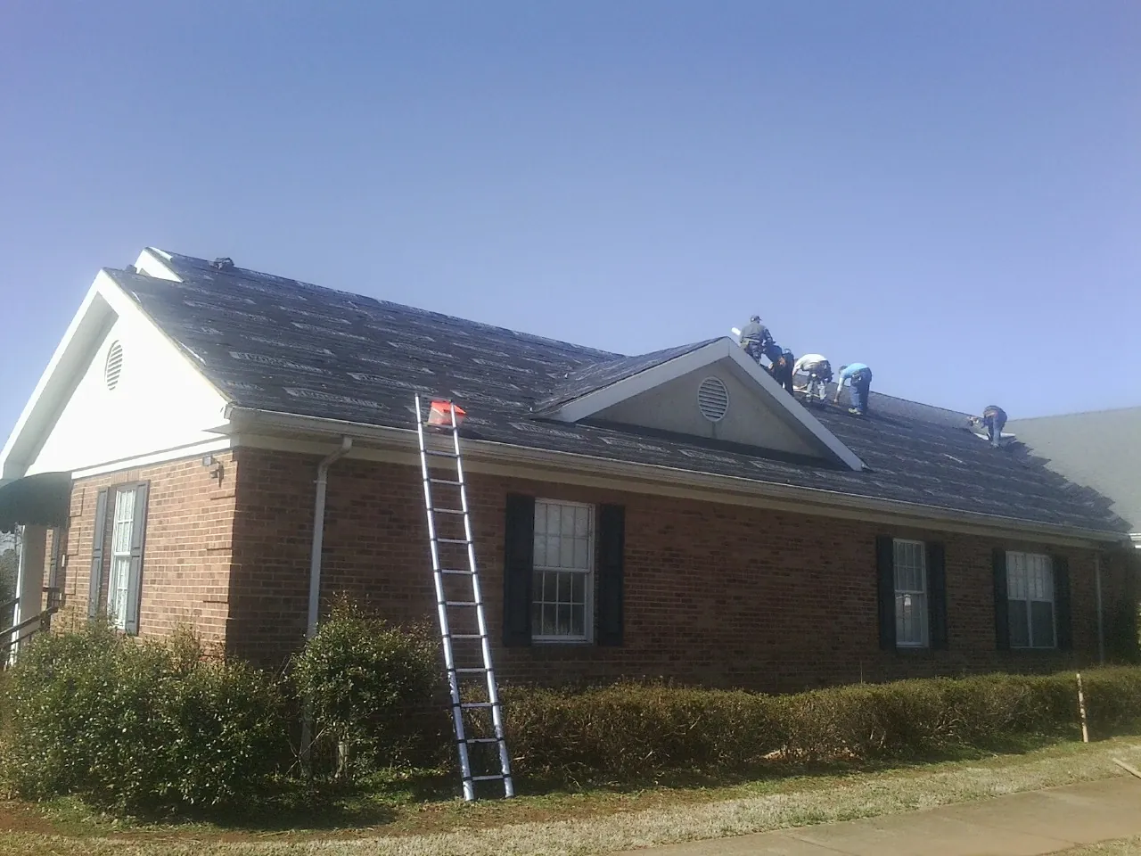 Crew tearing shingles off a brick ranch roof with a ladder set — Metal Roof Repair work by our crew in Jenkinsburg