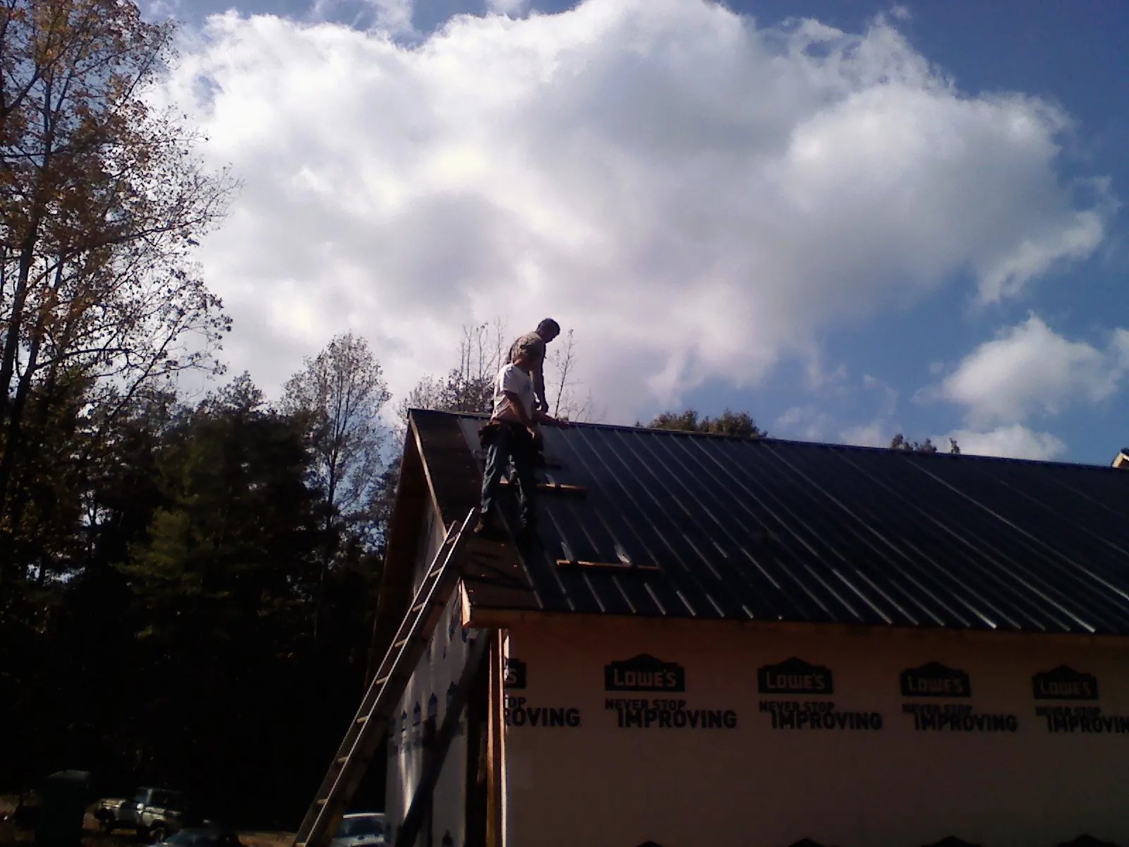Roofer fastening dark metal panels high against a cloudy sky, from a Roof Inspection job in Jenkinsburg
