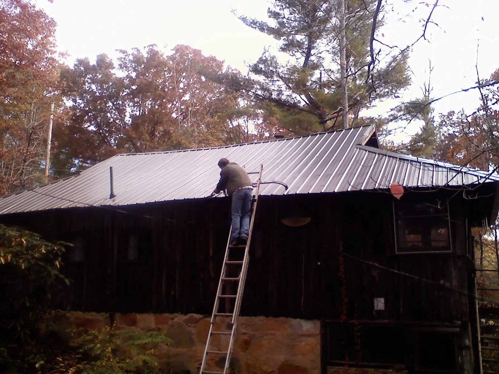 Roofer on a ladder working along the edge of a cabin metal roof in Jenkinsburg