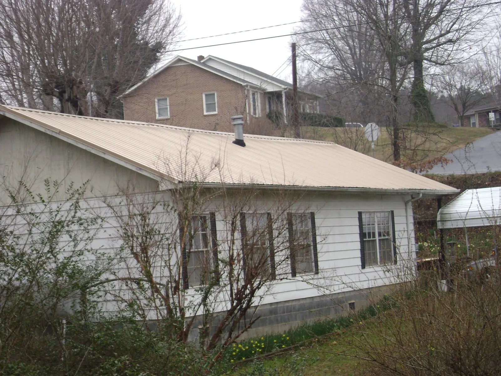 Tan metal roof on a white sided house set into a hillside — Commercial Roofing by Roofing Brothers in Jenkinsburg